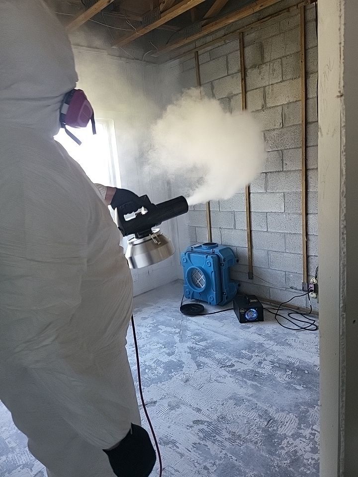 Technician in full PPE thermal fogging stripped room with air scrubber running